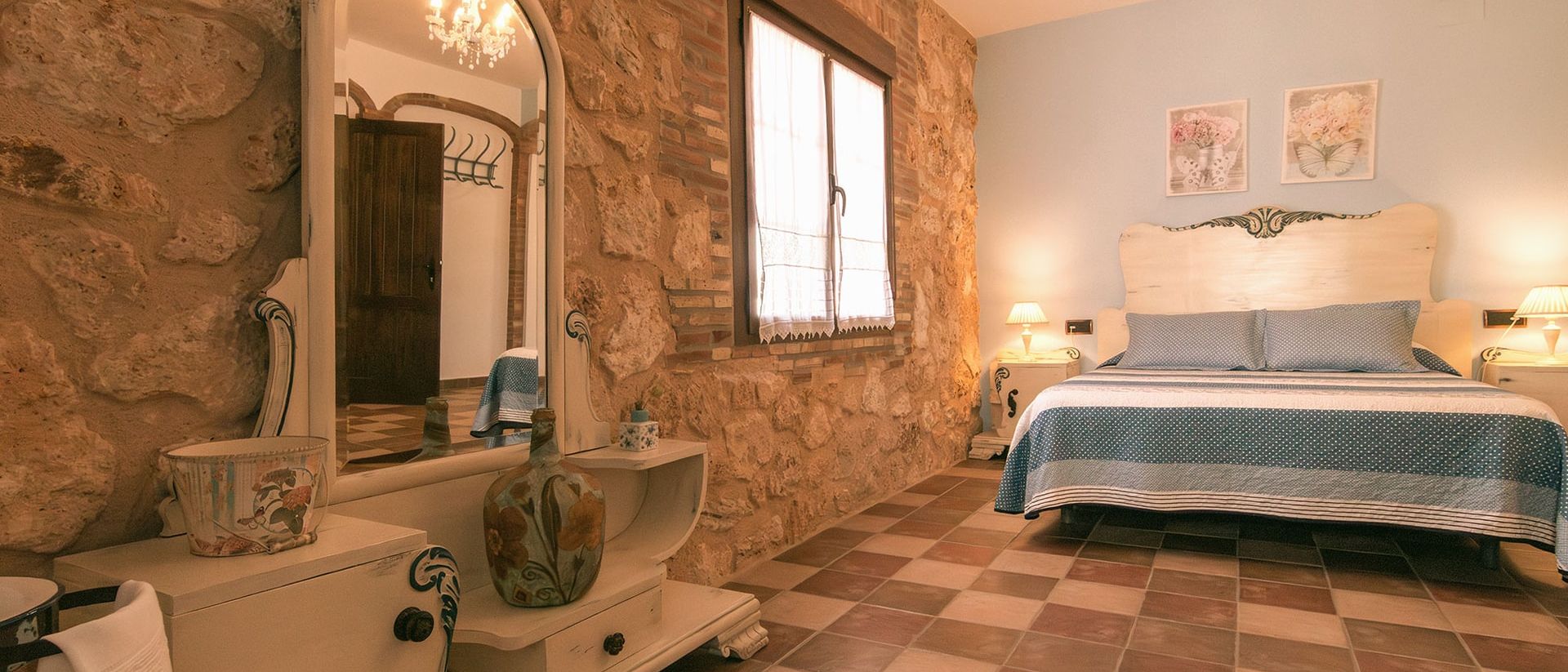 Dormitorio con muro de piedra, tocador blanco con espejo y cama doble