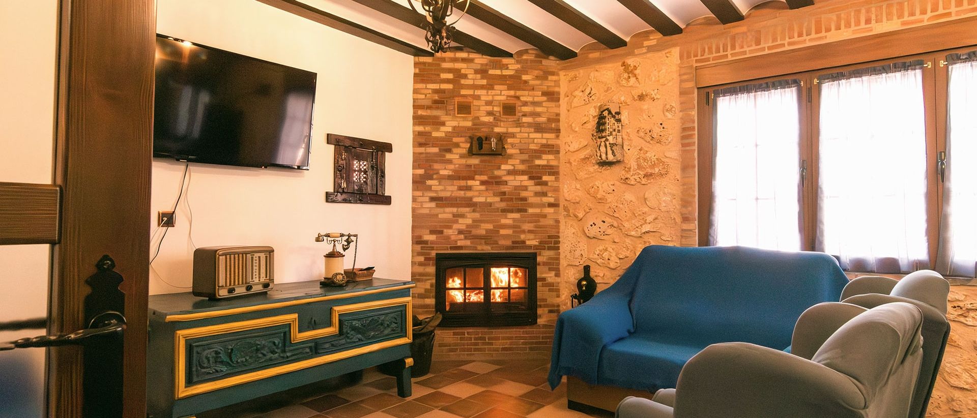 Salón con la chimenea encendida, sofá azul, butacas y techo de vigas de madera