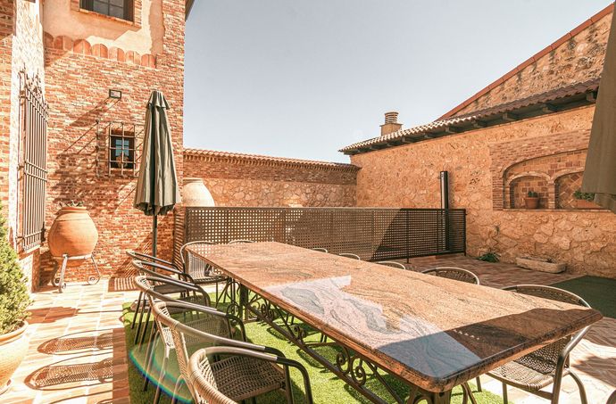 Terraza con una mesa larga, sillas y sombrilla entre muros de piedra